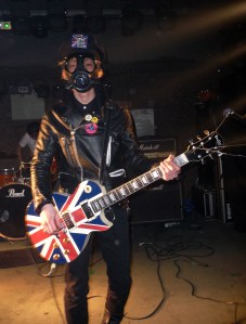 In a gas mask with a British guitar, no less